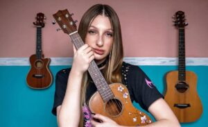 Yami Safdie posando con un ukelele decorado con flores, guitarras de fondo, cantante argentina de pop.