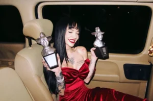 La Joaqui con vestido rojo en el interior de un auto posando con dos premio gardel 2025