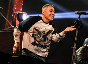 El Loco Amato durante un show en vivo, sonriendo y gesticulando, con remera de manga larga blanca y negra frente al micrófono con el número 22.