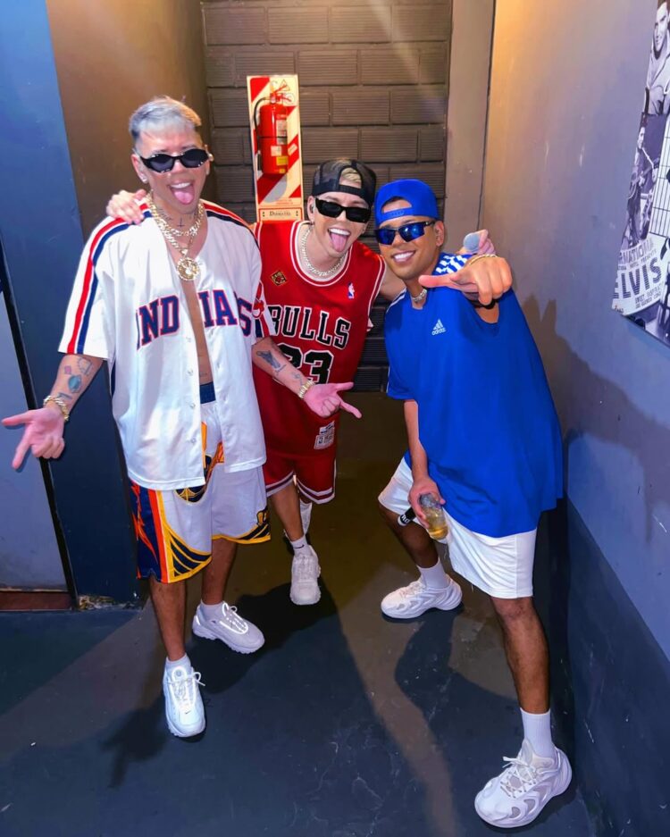 Los Nota Lokos posando con estilo urbano en pasillo con camisetas de básquet y cadenas de oro