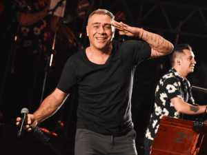El Loco Amato saludando al público en un recital, con remera negra y micrófono en mano, acompañado por su banda