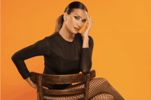 Momi Giardina en una producción fotográfica con fondo naranja, look elegante en negro y medias de red.