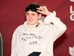 Dillom en la alfombra roja de los Latin Grammy con un buzo blanco y estampa que indica: "Grammy Latinos en USA..."